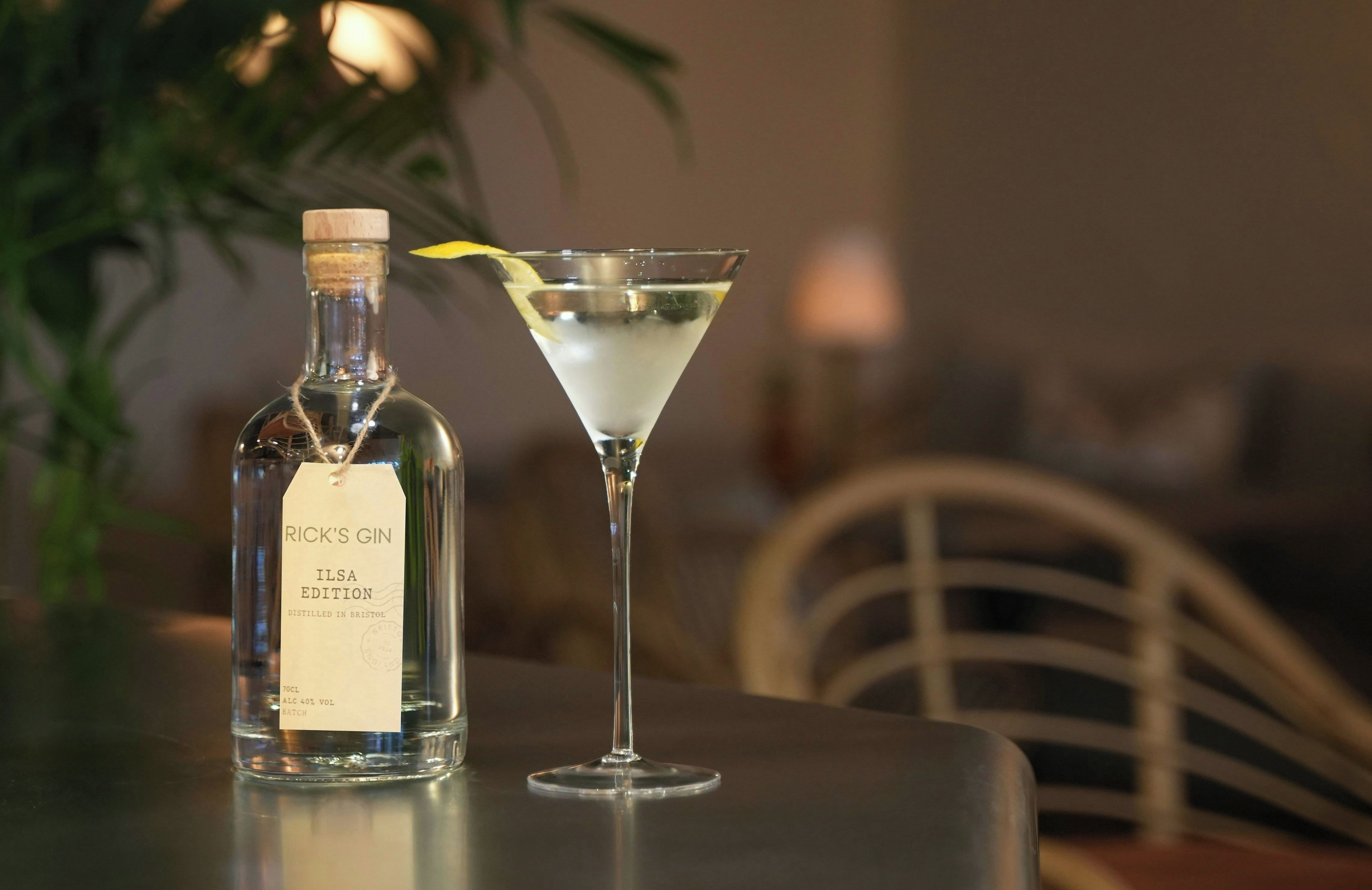 A bottle of Rick's Gin ILSA Edition and a martini glass with a lemon twist on a table.