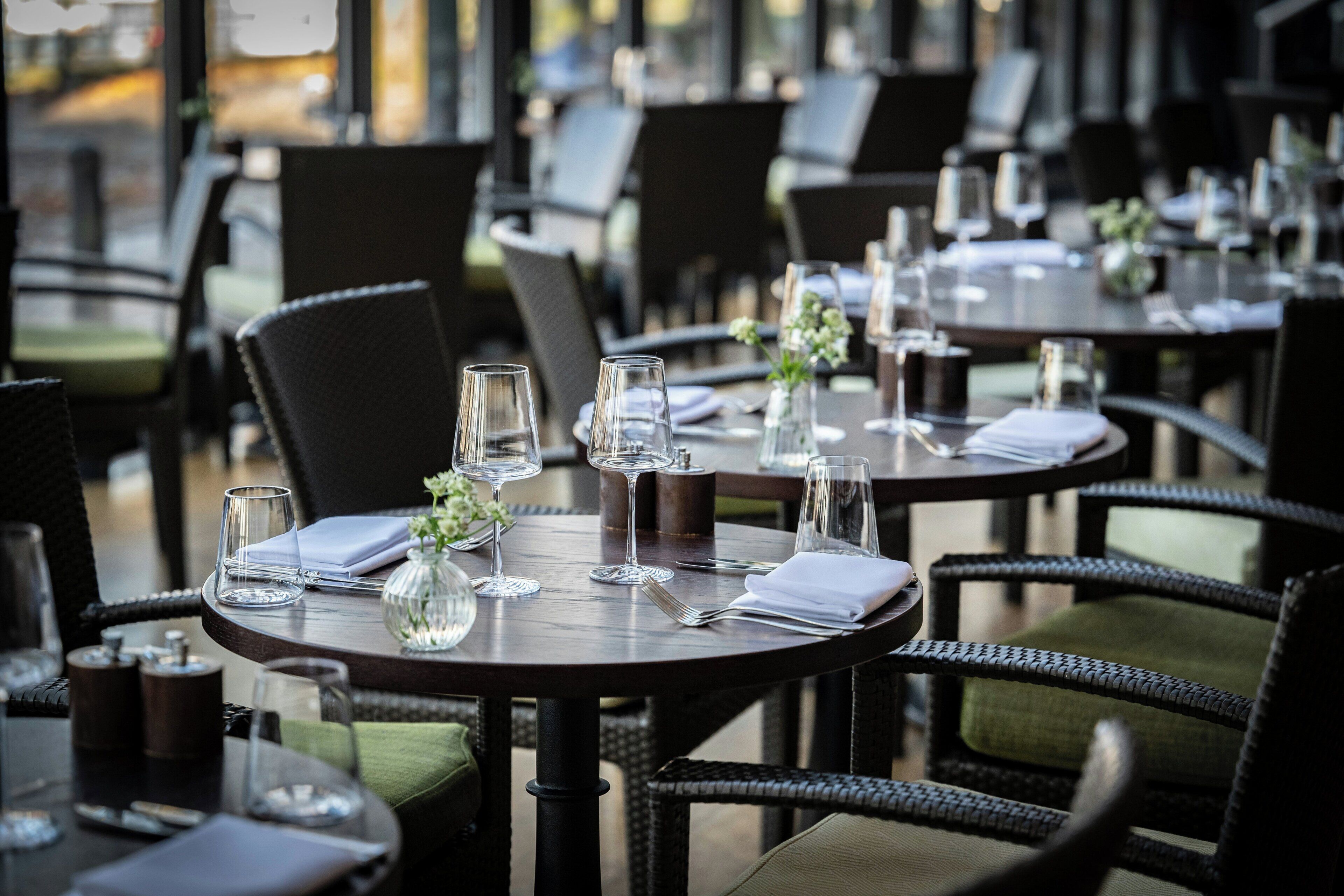 Un restaurante con mesas redondas, sillas y copas de vino vacías.