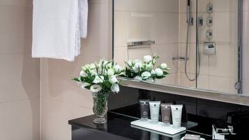 A modern bathroom with a large mirror, a white towel, a vase of flowers, and toiletries on the counter.