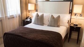 A hotel room with a large bed, two bedside tables, a nightstand, a lamp, and a window with curtains.
