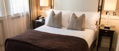 A hotel room with a large bed, two bedside tables, a nightstand, a lamp, and a window with curtains.