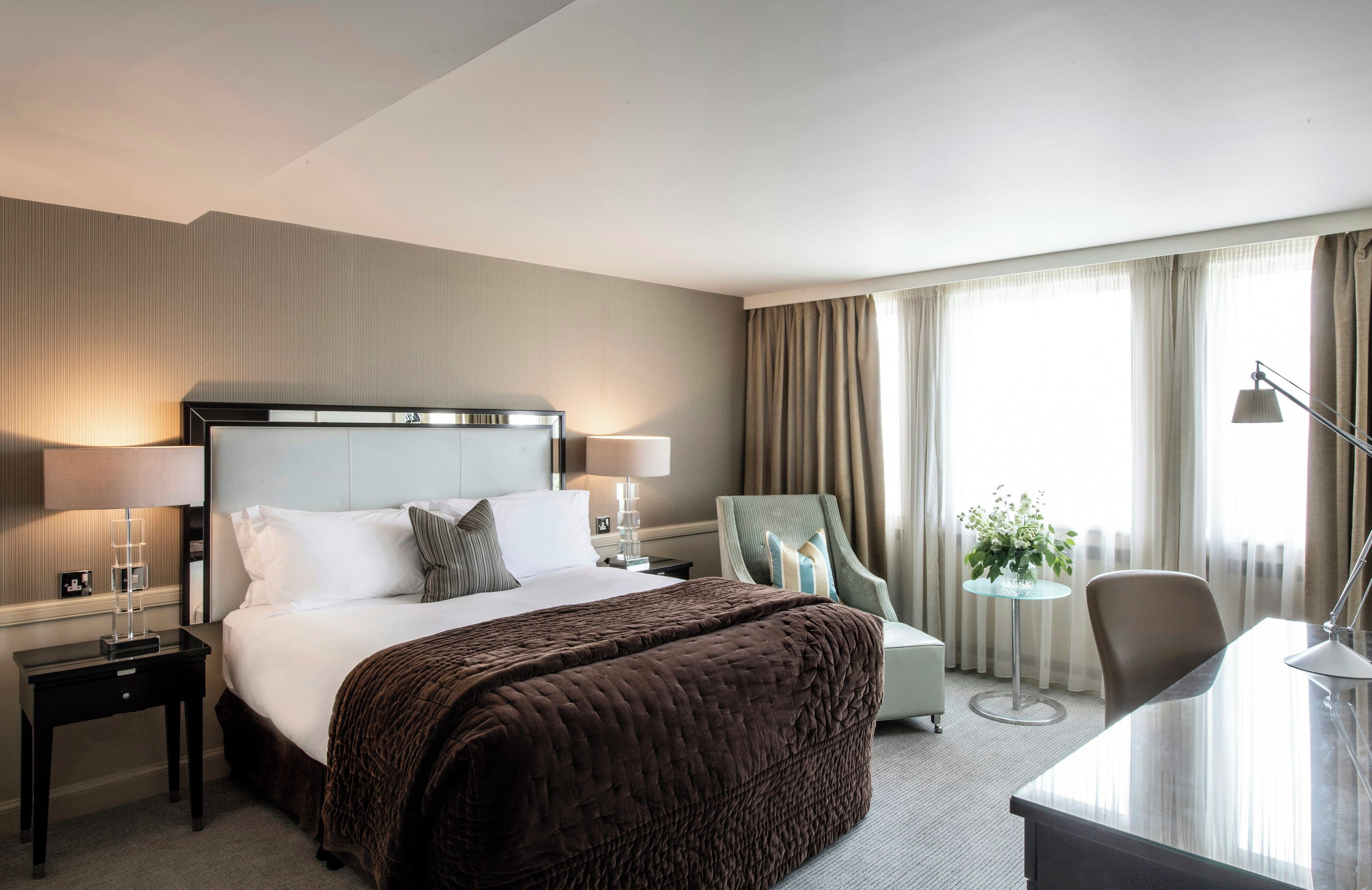 Una habitación de hotel con una cama grande, mesitas de noche, un escritorio, una silla y una ventana con cortinas.