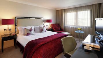 Habitación de hotel con cama, escritorio con silla, televisor y ventana con cortinas.