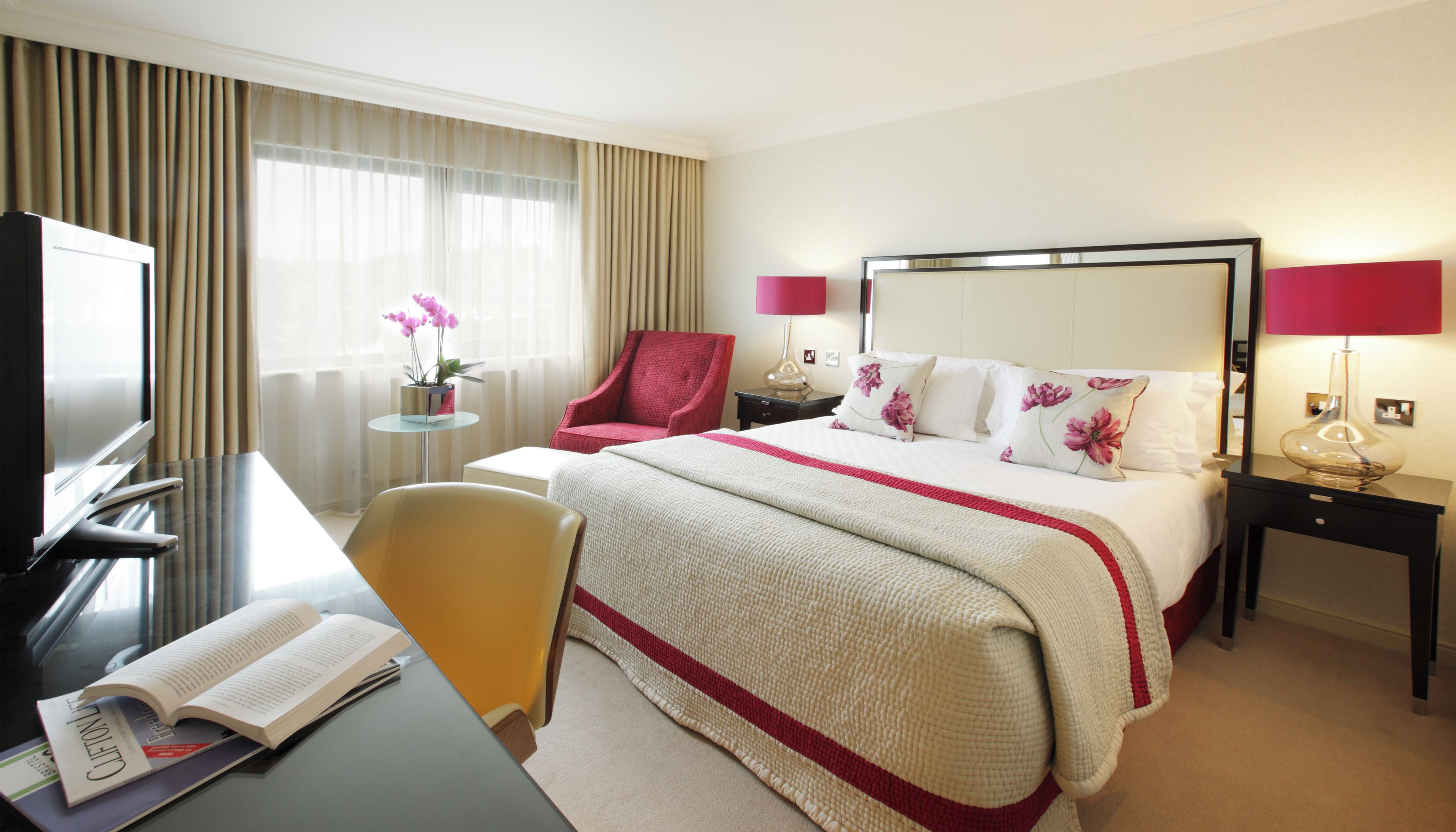 Une chambre d’hôtel avec un lit, un bureau et une chaise, une télévision et une fenêtre avec des rideaux.