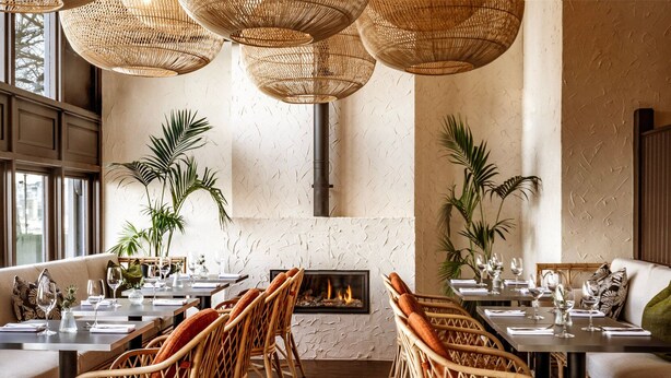 Een restaurant met rieten meubels, een open haard en grote ramen.