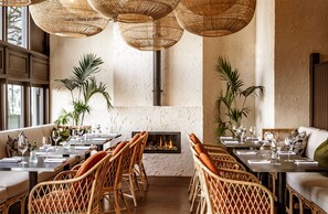 A restaurant with wicker furniture, a fireplace, and large windows. - The Bristol Hotel (Bristol)
