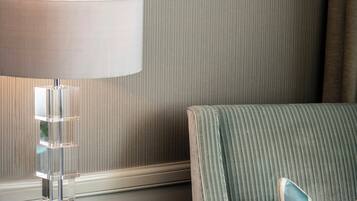 Una camera d'albergo con un letto, un comodino con una lampada, una sedia con un cuscino e una parete a righe.