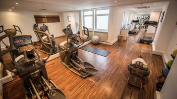 A home gym with various exercise equipment, a wooden floor, and large windows providing natural light.