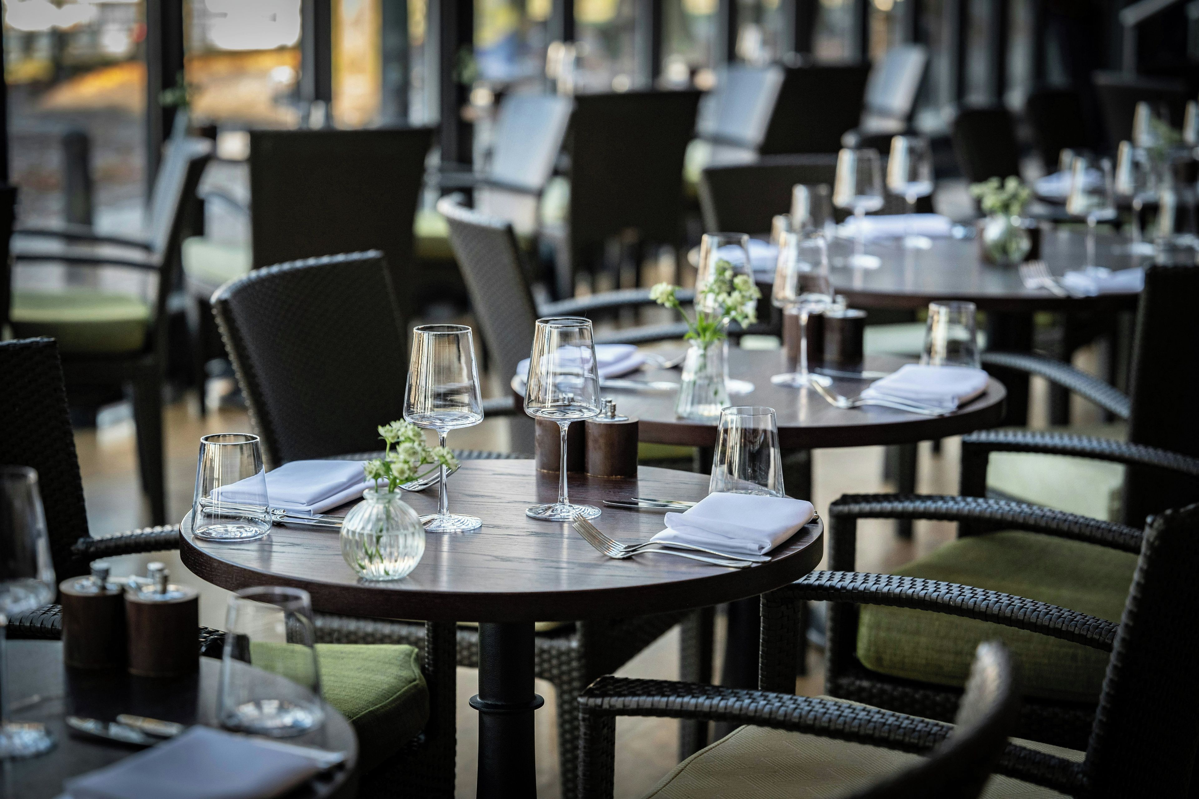 Une salle de restaurant avec des tables rondes, des chaises et des verres à vin vides.