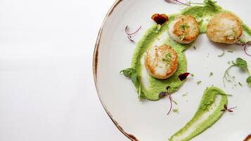 A plate with seared scallops, green sauce, and microgreens.