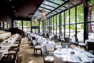 A restaurant with long tables and chairs, large windows, and hanging light fixtures.