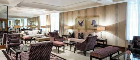 A spacious hotel lobby with a central seating area, a coffee table, and a large mirror.