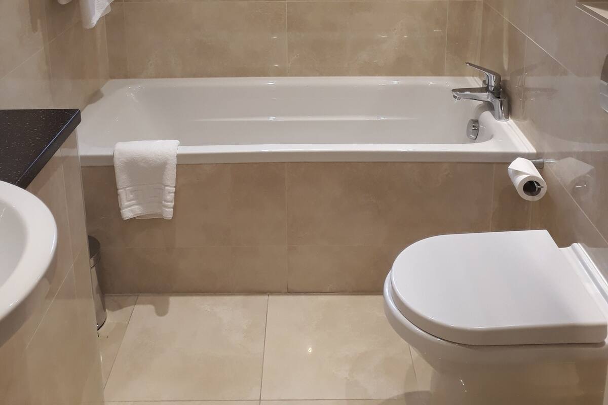 A modern bathroom with a bathtub, toilet, and a window.