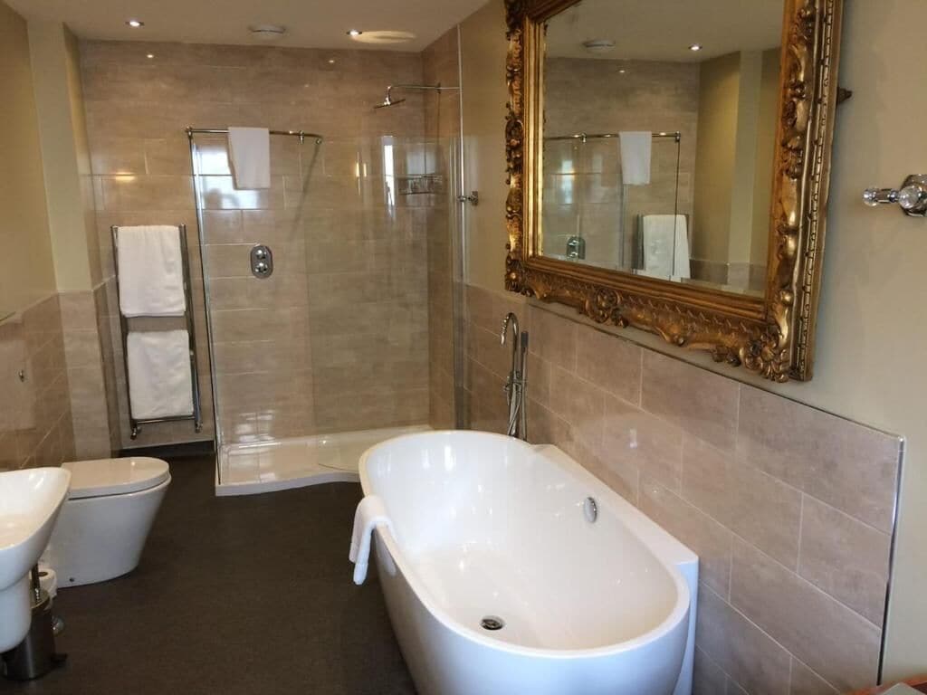 A modern bathroom with a freestanding bathtub, a glass-enclosed shower, and a large mirror with an ornate frame.