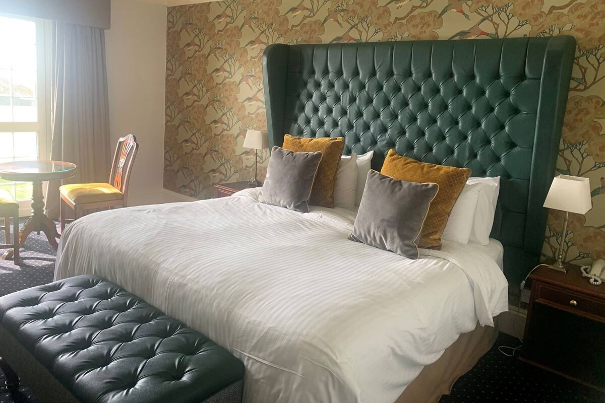 A hotel room with a large bed, a tufted headboard, a bench, a chair, and a small table.