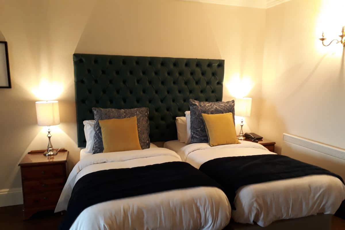 A double bed with a tufted headboard, two bedside tables with lamps, and a nightstand with a telephone.