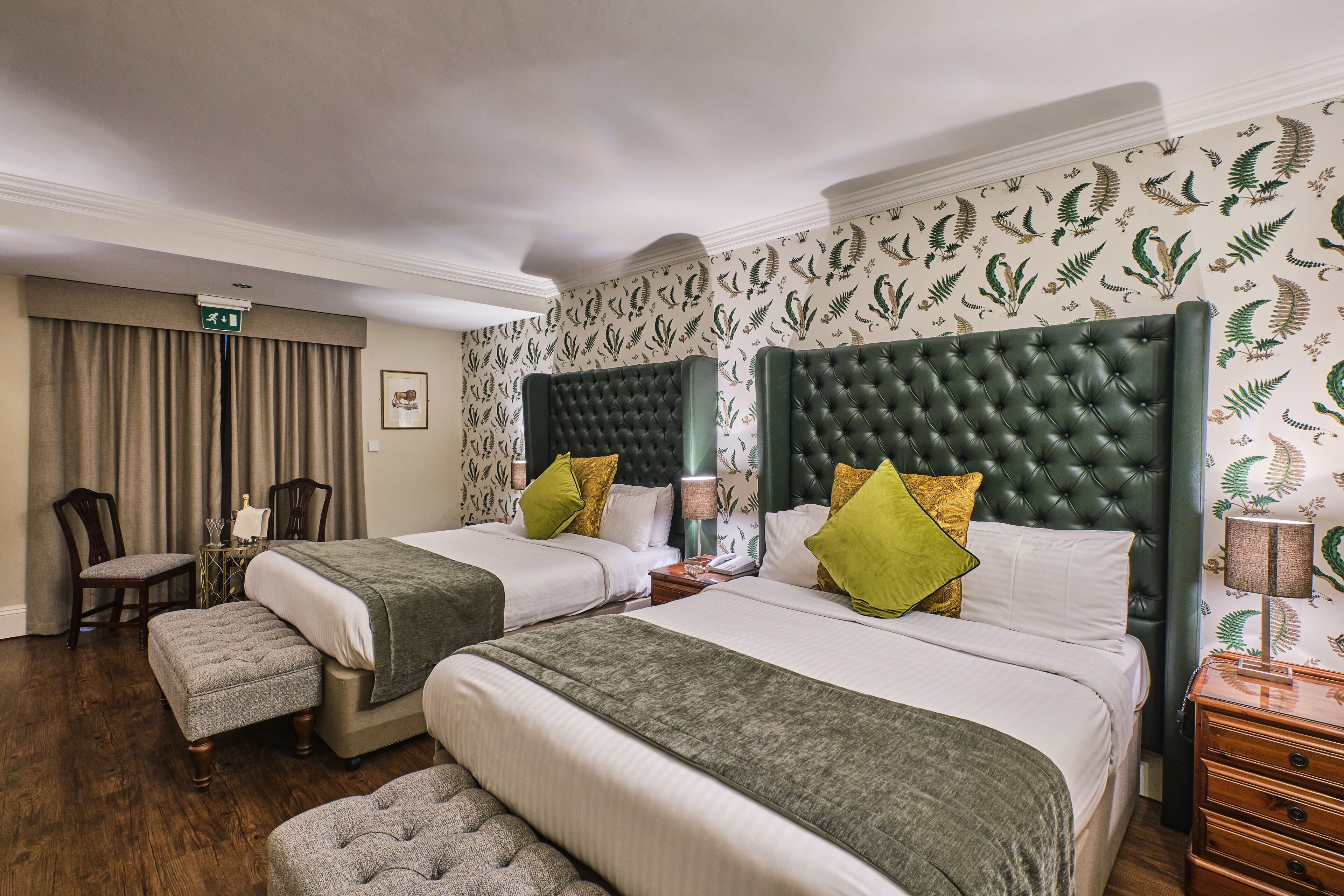 A hotel room with two beds, a sitting area, and a view of the hallway.