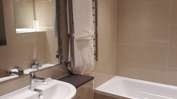 Un baño moderno con lavamanos, espejo, toallero y bañera.