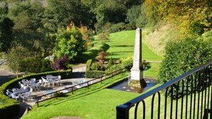 A landscaped garden with a stone obelisk, a paved patio with tables and chairs, and a grassy lawn. - New House Country Hotel (Cardiff)