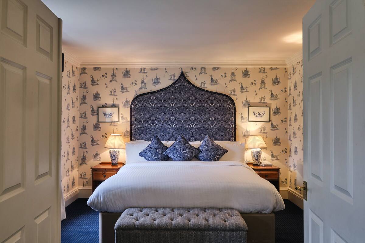 A neatly made bed with a decorative headboard, two bedside lamps, and a matching bench.