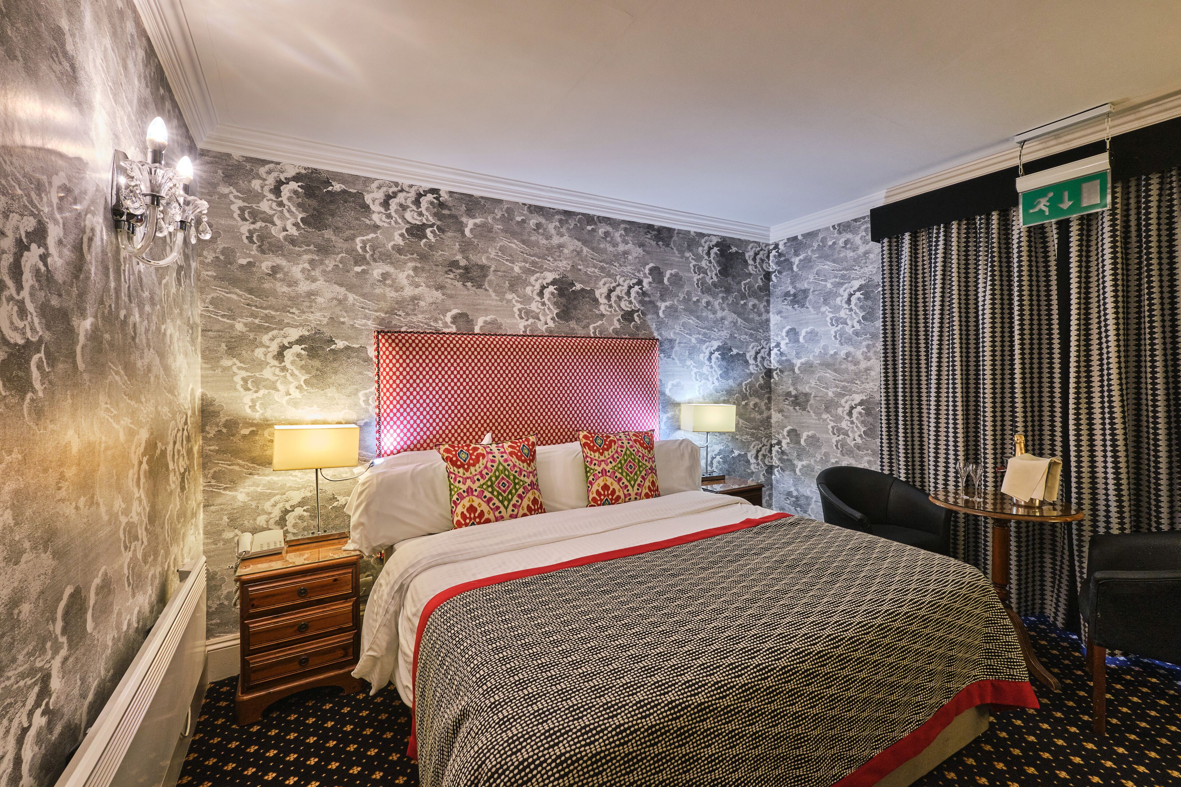 Una habitación de hotel con una cama, una mesita de noche, una lámpara, una silla y una pared con textura.