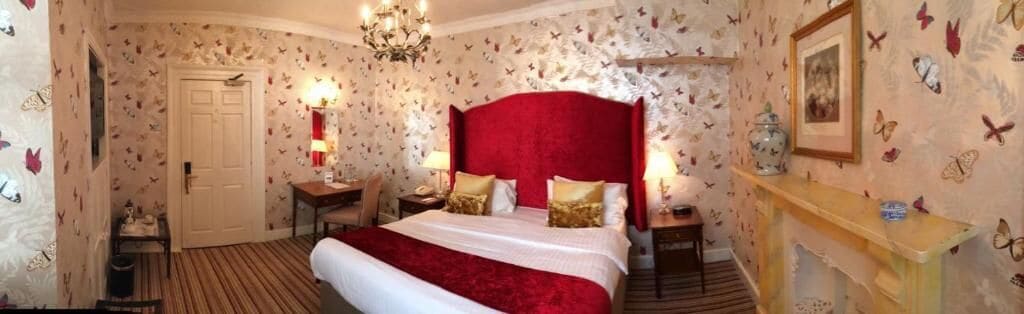 A bedroom with a large bed, a chandelier, a nightstand, a dresser, and butterfly wallpaper.