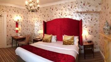 A bedroom with a large bed, a chandelier, a nightstand, a dresser, and butterfly wallpaper.