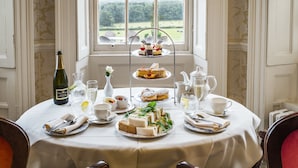 A table set for a tea service with sandwiches, cakes, and a bottle of wine, overlooking a garden. - New House Country Hotel (Cardiff)
