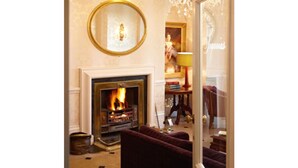 A cozy living room with a fireplace, a round mirror, and a chandelier. - New House Country Hotel (Cardiff)