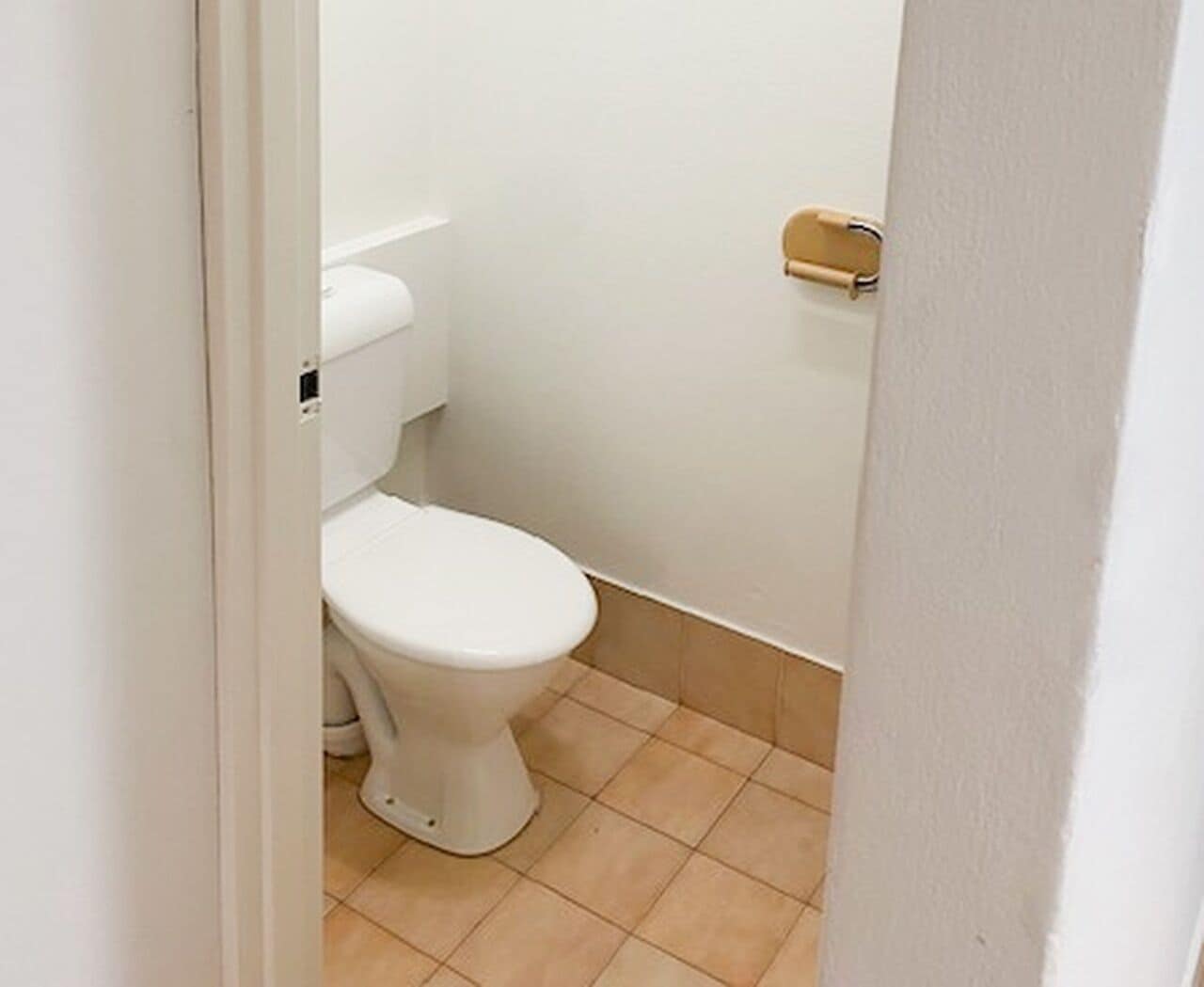 A small, white toilet in a narrow bathroom with beige tiles.