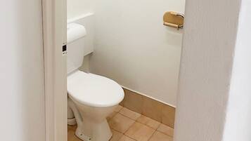 Un inodoro pequeño y blanco en un baño estrecho con azulejos color beige.