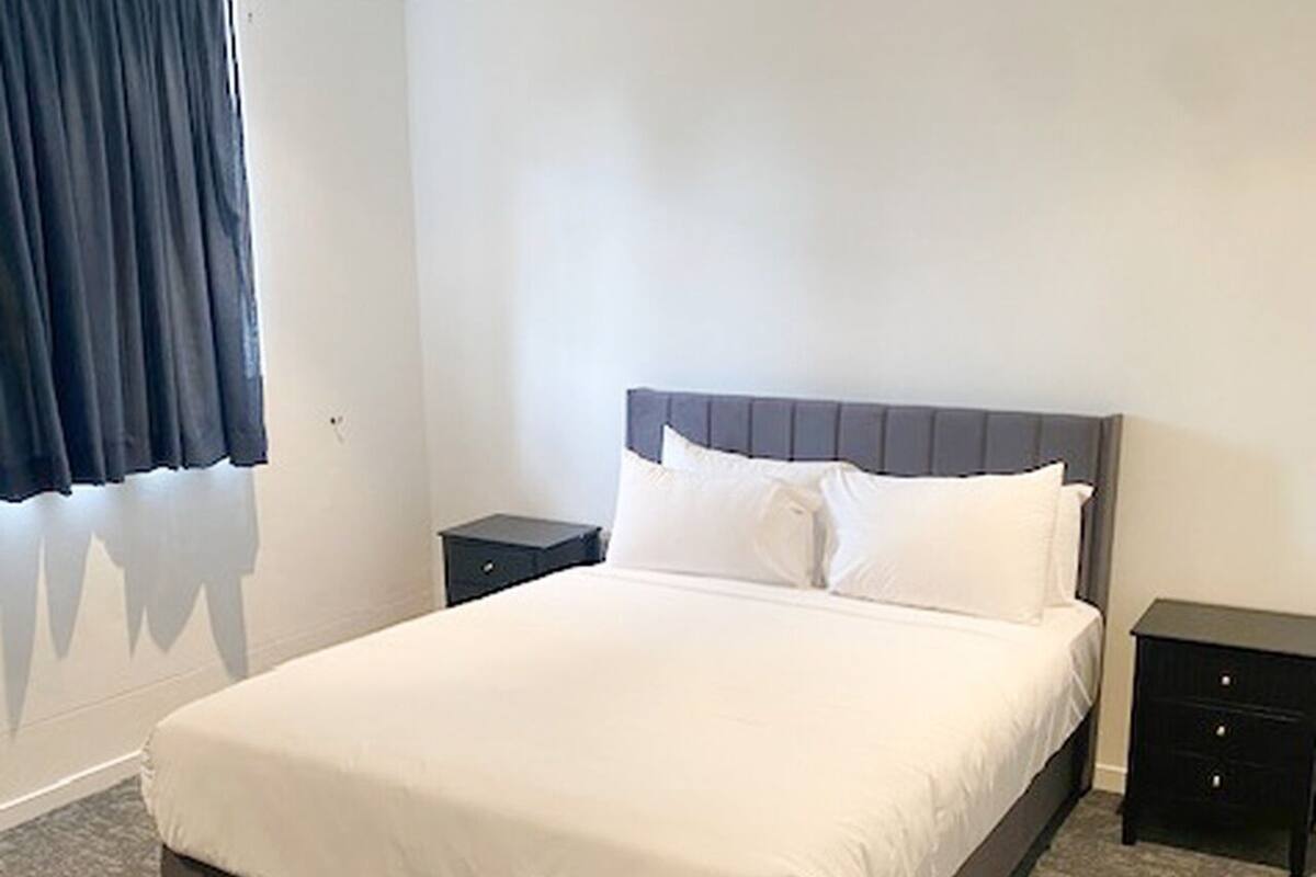 A neatly made bed with white linens, two bedside tables, and a dark headboard.