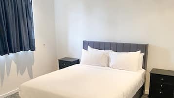 Un lit bien fait, avec du linge de lit blanc, deux tables de chevet et une tête de lit sombre.