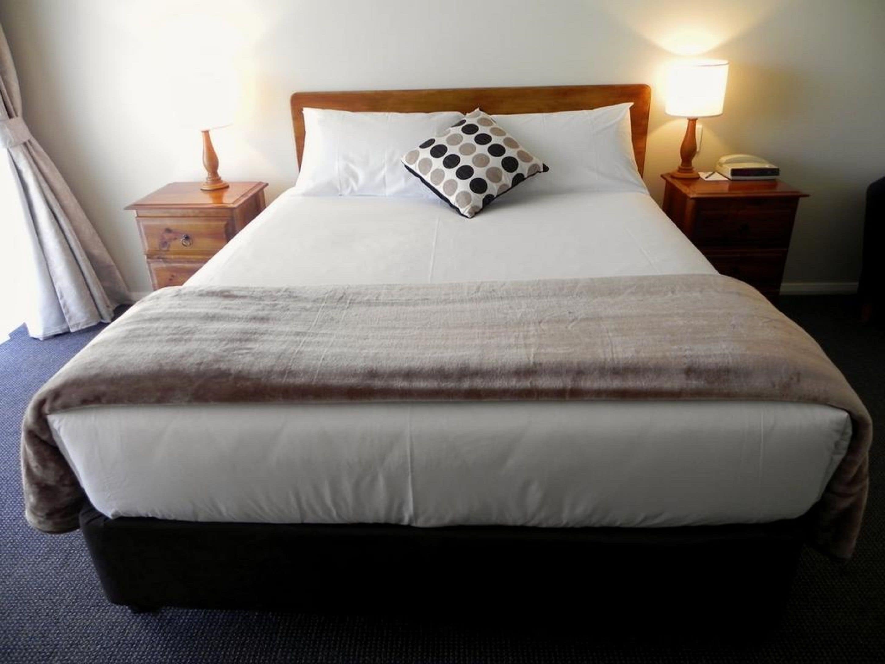 A neatly made bed with a white duvet and a polka dot pillow, flanked by wooden nightstands with lamps.