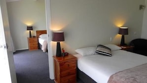 A hotel room with a single bed, two bedside tables with lamps, a wooden dresser, and a door leading to another room. - Moore Park Inn (Armidale)