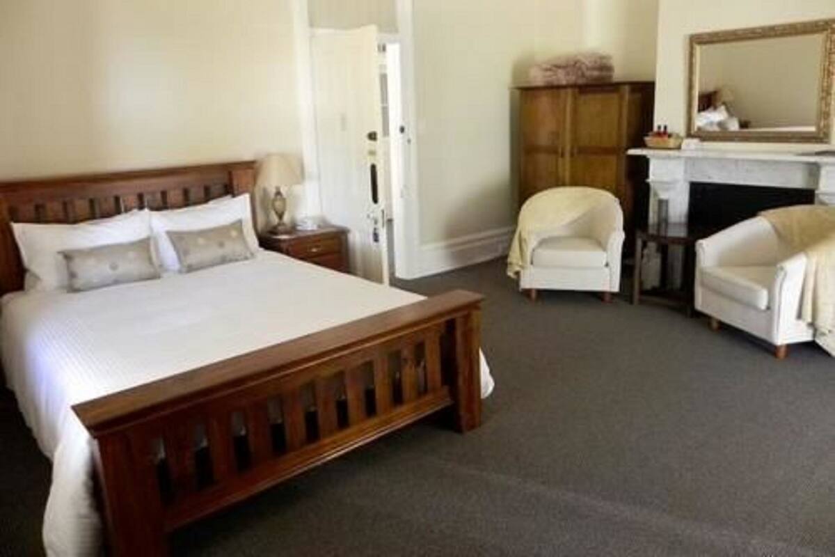 A bedroom with a wooden bed, a chair, a desk, and a mirror.