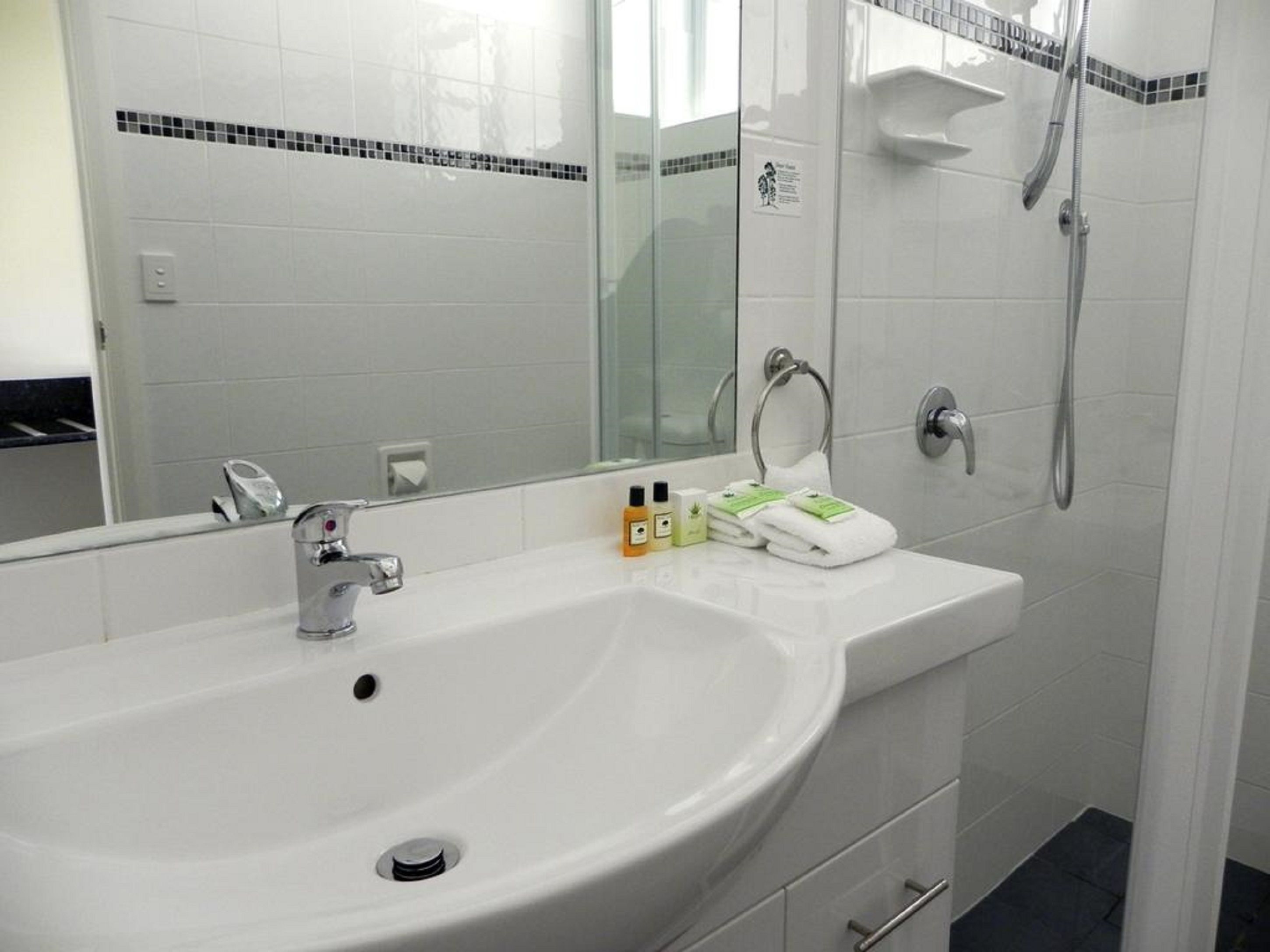 A modern bathroom with a white sink, a large mirror, and a shower.