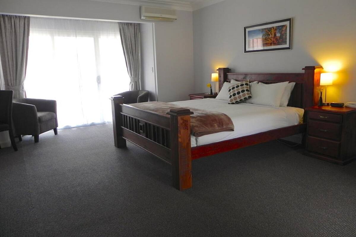A hotel room with a bed, a chair, a nightstand, and a window with curtains.
