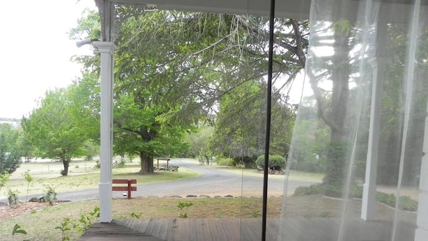 A covered outdoor area with a bench, a pathway, and a view of a road and trees. - Moore Park Inn (Armidale)