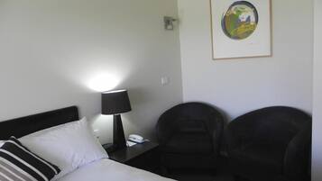 A hotel room with a bed, a bedside lamp, a telephone, and two chairs.
