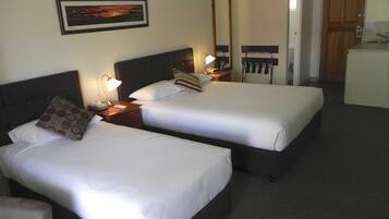 A hotel room with two beds, a nightstand with a lamp, a mirror, and a view of a kitchen area.