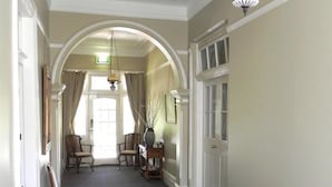 A hallway with a red sofa, a wooden table with glasses, and a chandelier. - Moore Park Inn (Armidale)