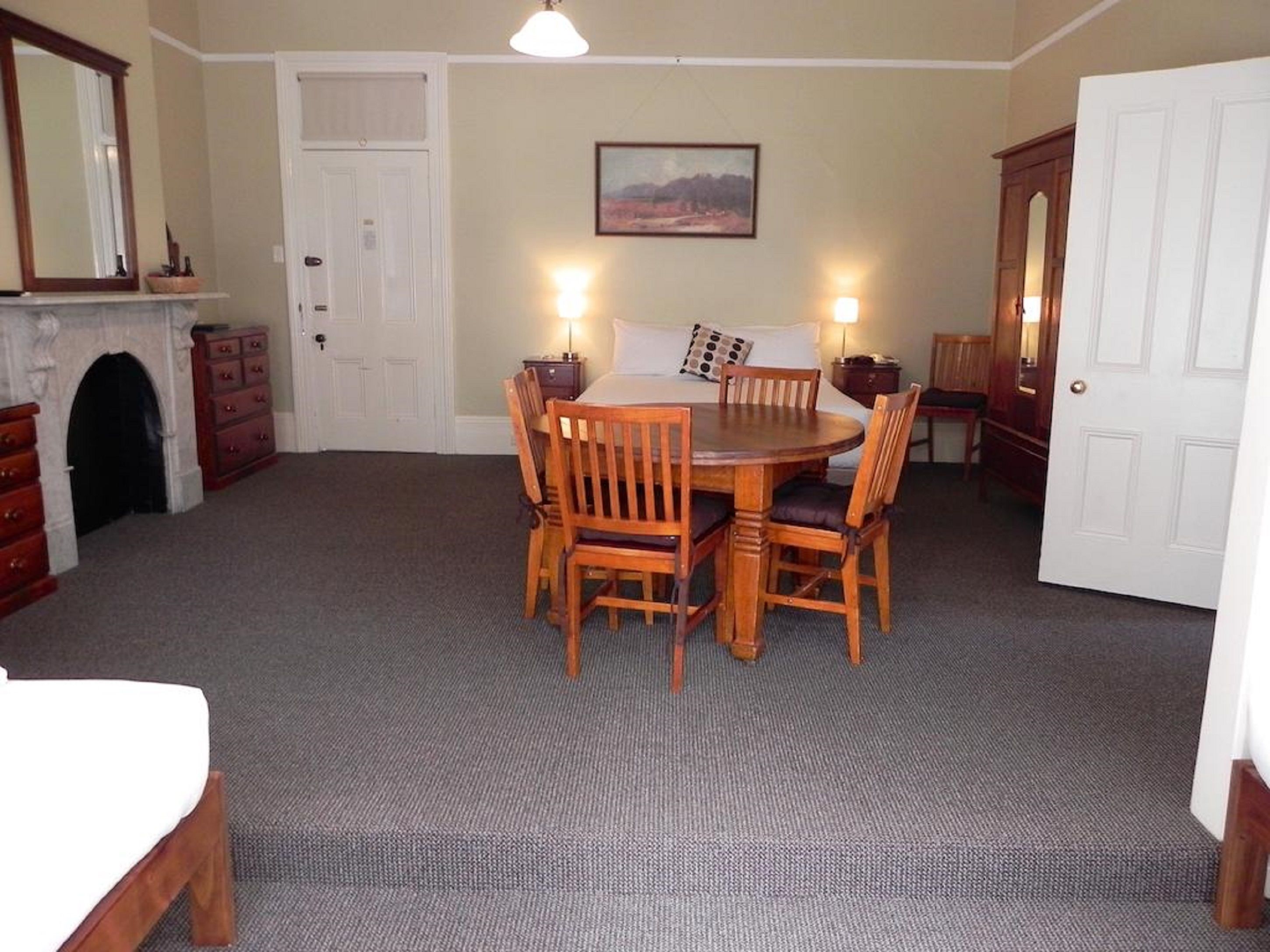 A dining area with a round wooden table and chairs, a fireplace, a door, and a framed picture on the wall.