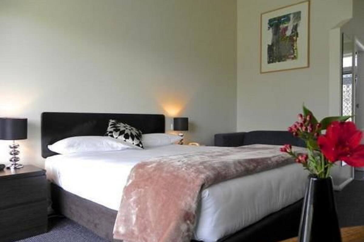 A bedroom with a bed, bedside tables, a nightstand, a vase with flowers, and a painting on the wall.
