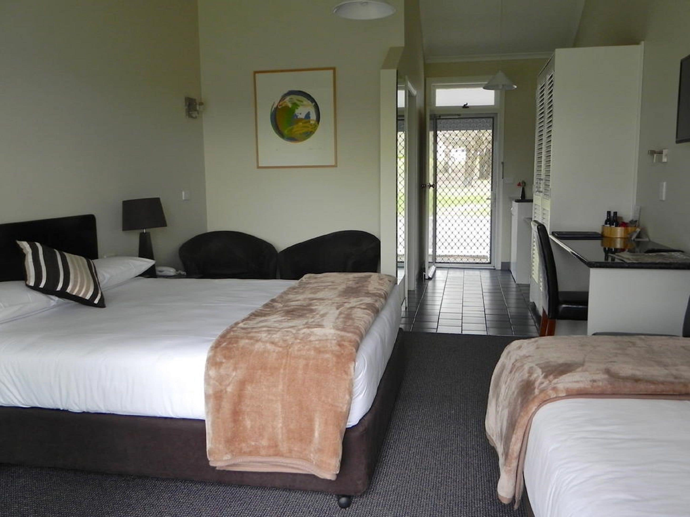 Een hotelkamer met twee bedden, een bureau, een stoel, een lamp en een deur naar een balkon.