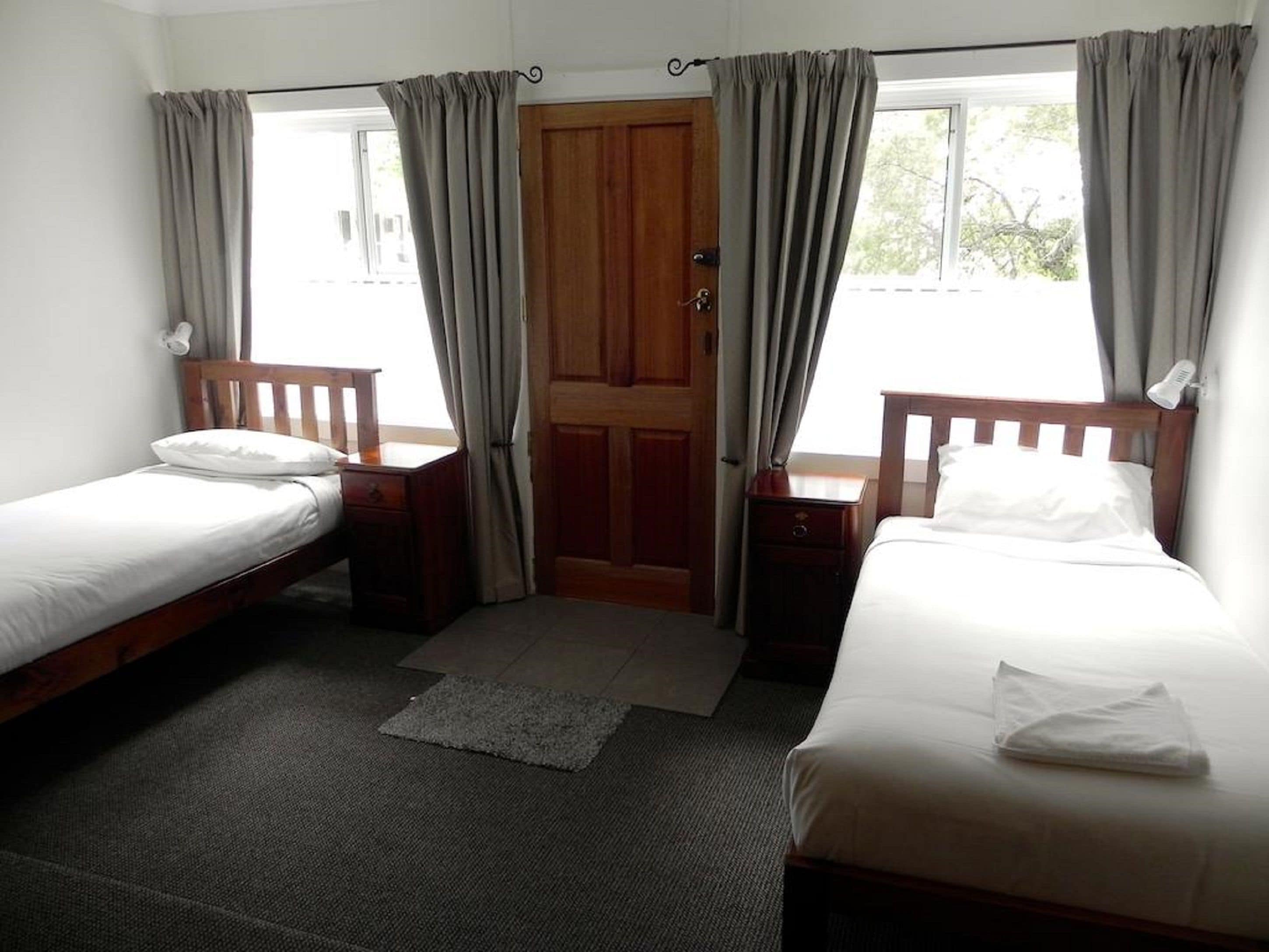 A room with two single beds, a wooden door, and a window with curtains.