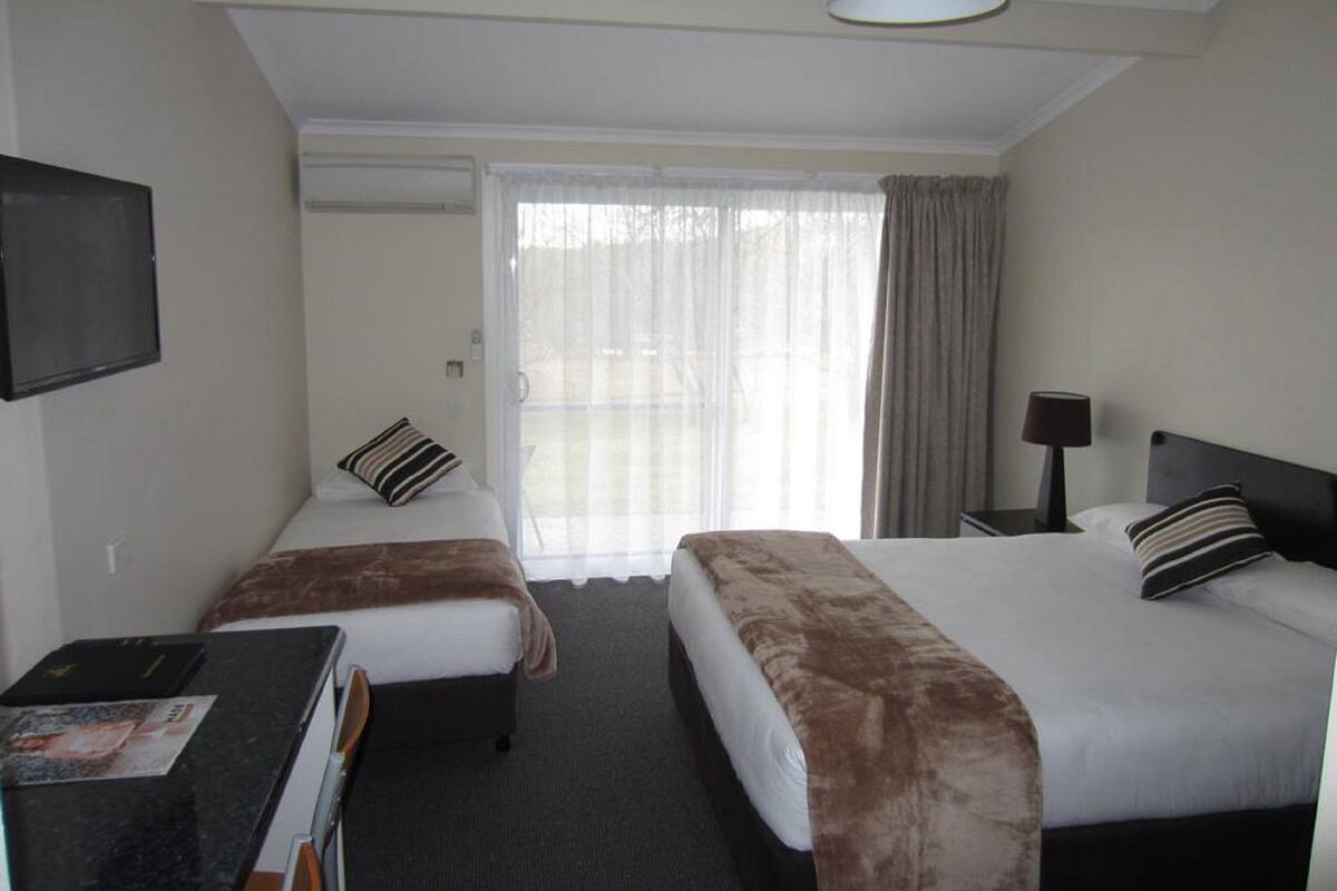 A hotel room with two beds, a desk, a TV, and a window with curtains.