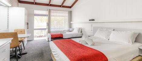 A hotel room with a bed, a desk, and a chair. There is a window with curtains and a view of the outside.