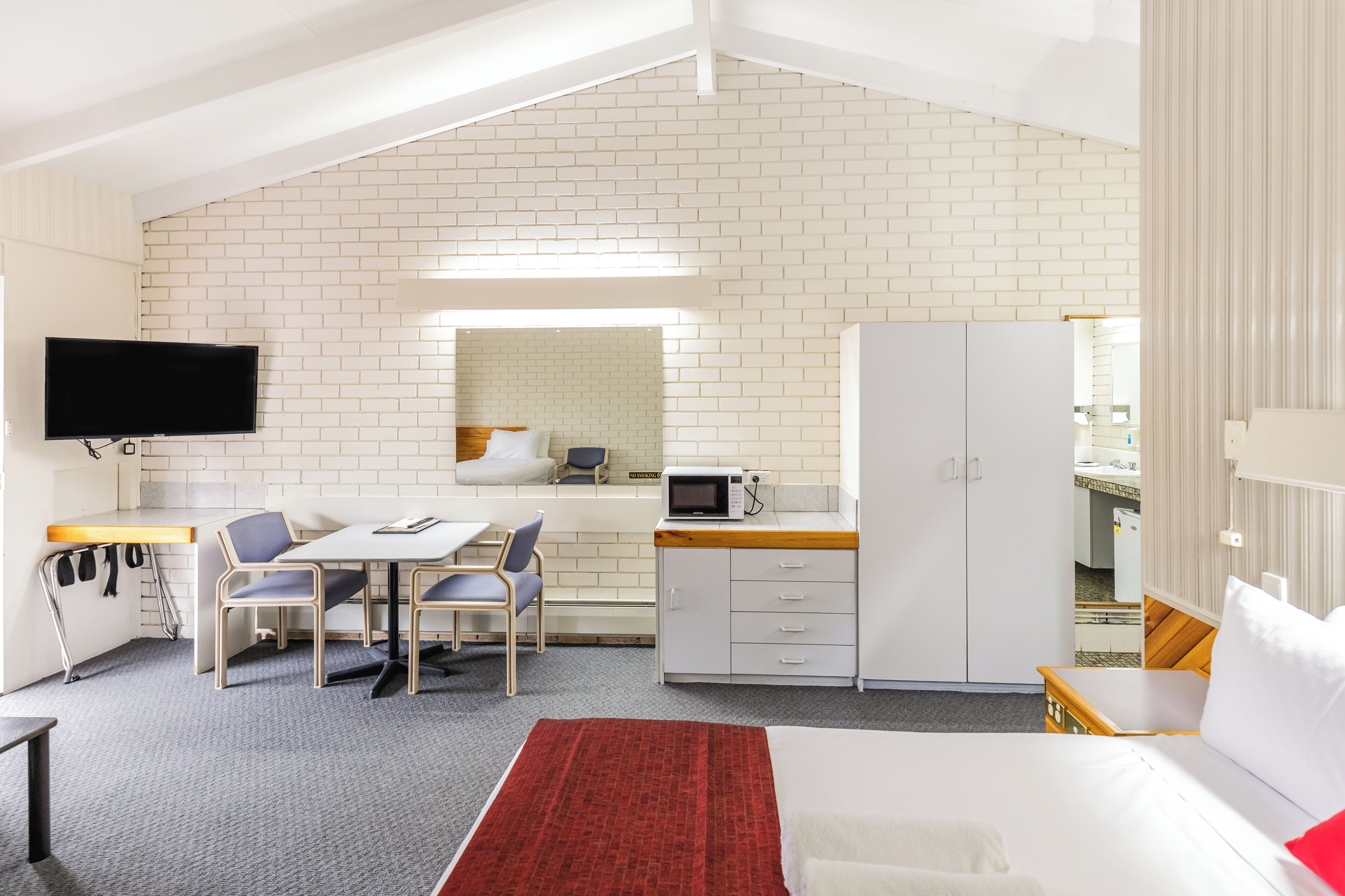 Une chambre de taille réduite comprenant un lit, un bureau avec une chaise, un four à micro-ondes et un téléviseur fixé au mur.