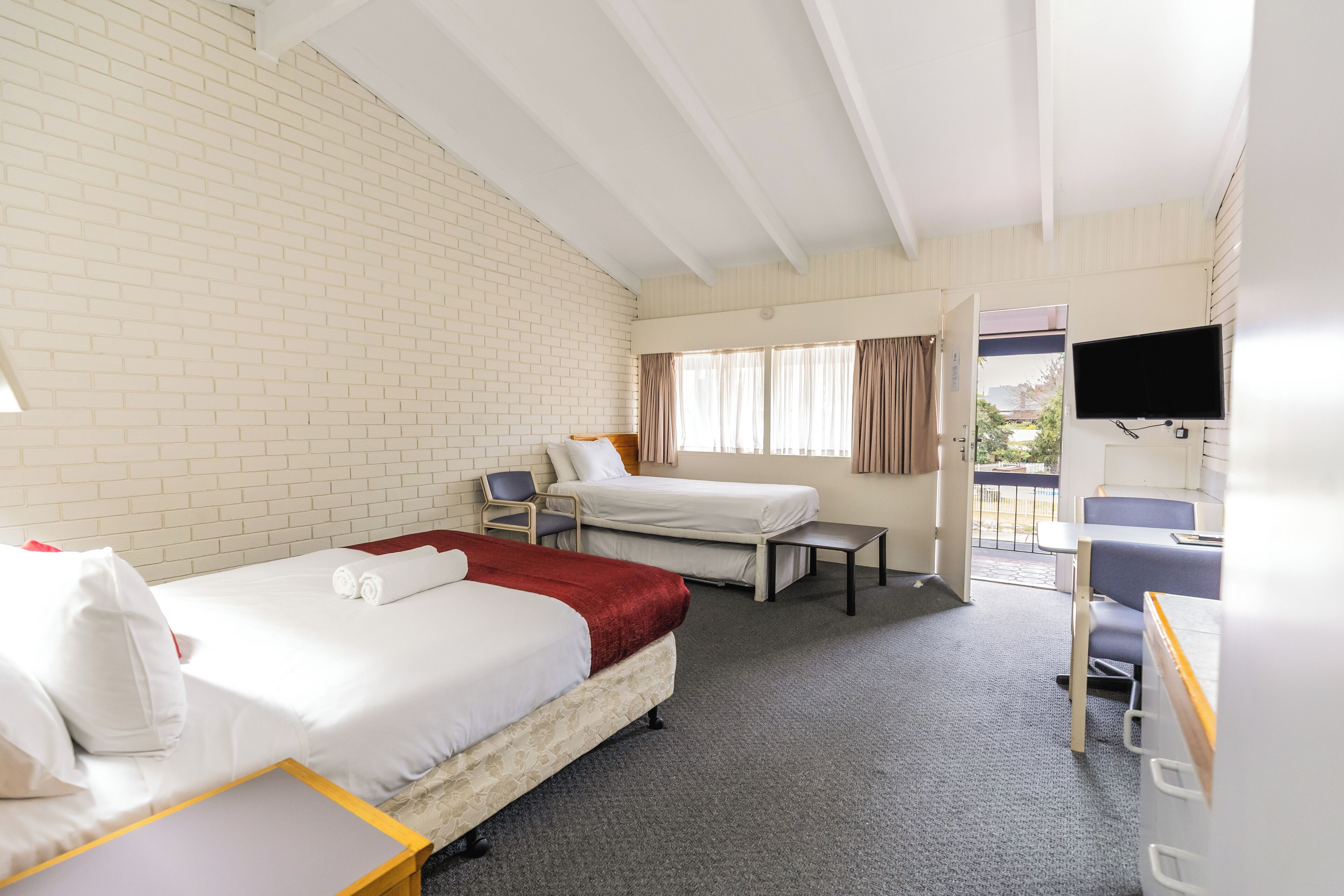 A hotel room with two beds, a desk, a chair, a TV, and a window with curtains.